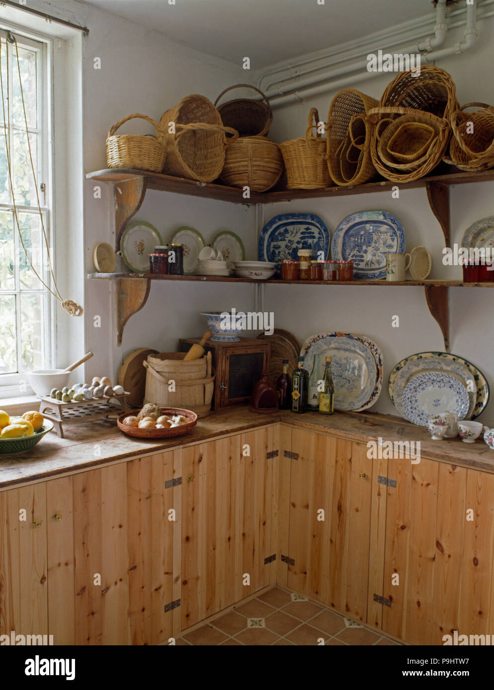 Collection of vintage baskets and crockery on simple shelves in nineties kitchen with pine cupboards Stock Photo