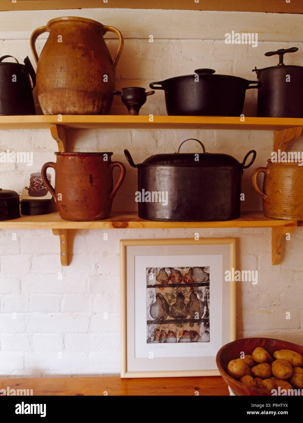 Collection of earthenware and cast-iron pots on simple wooden shelves in kitchen Stock Photo