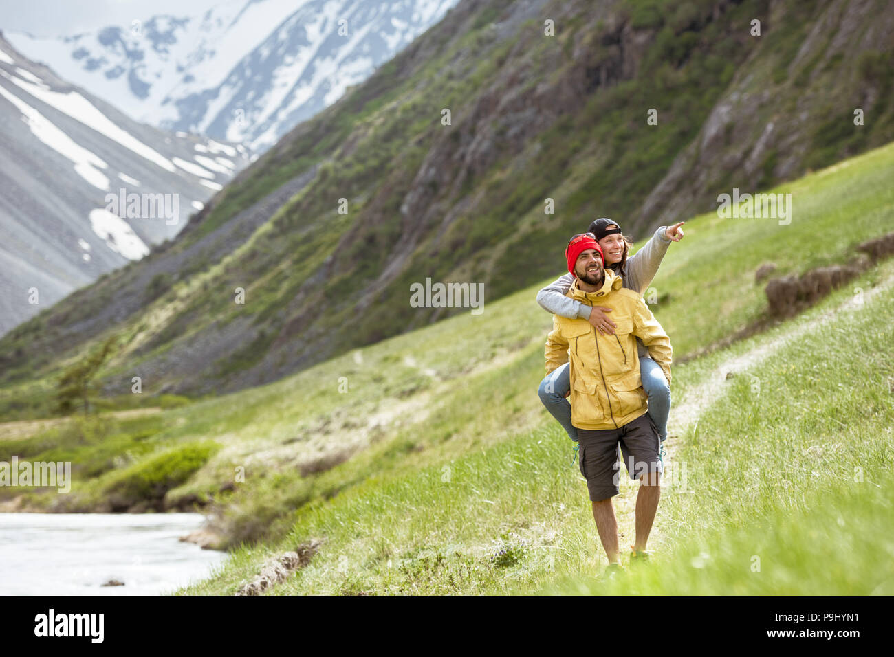 Happy couple is having fun in mountains area. Girl rides piggyback and smiling Stock Photo