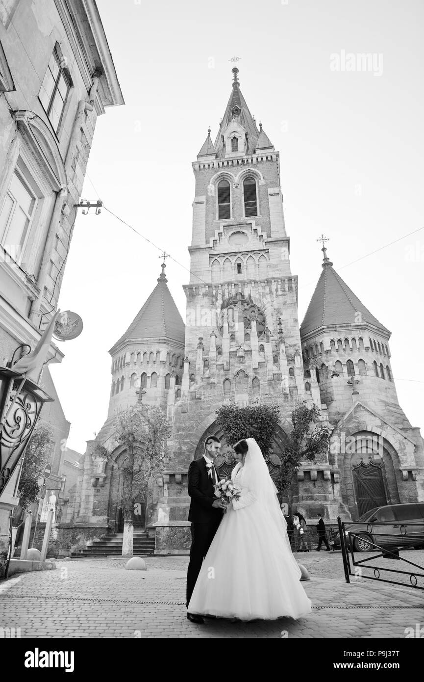 Newly married couple posing next to the old church in the town on a beautiful autumn wedding day. Stock Photo