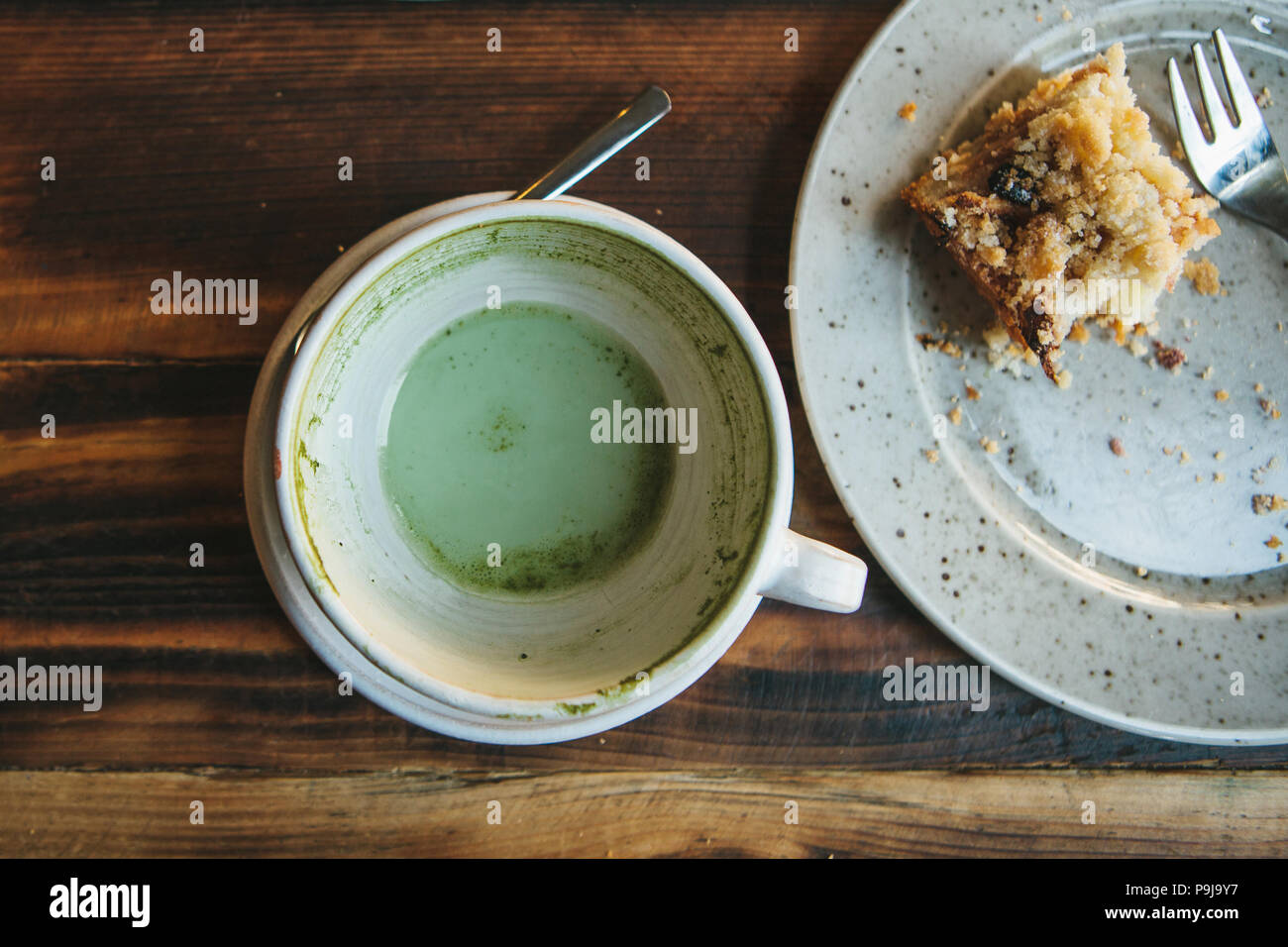 Top view. A dirty plate and an empty cup of Matcha tea. The half-eaten cupcake on a plate. Empty dishes after eating on a wooden table in a cafe. The  Stock Photo