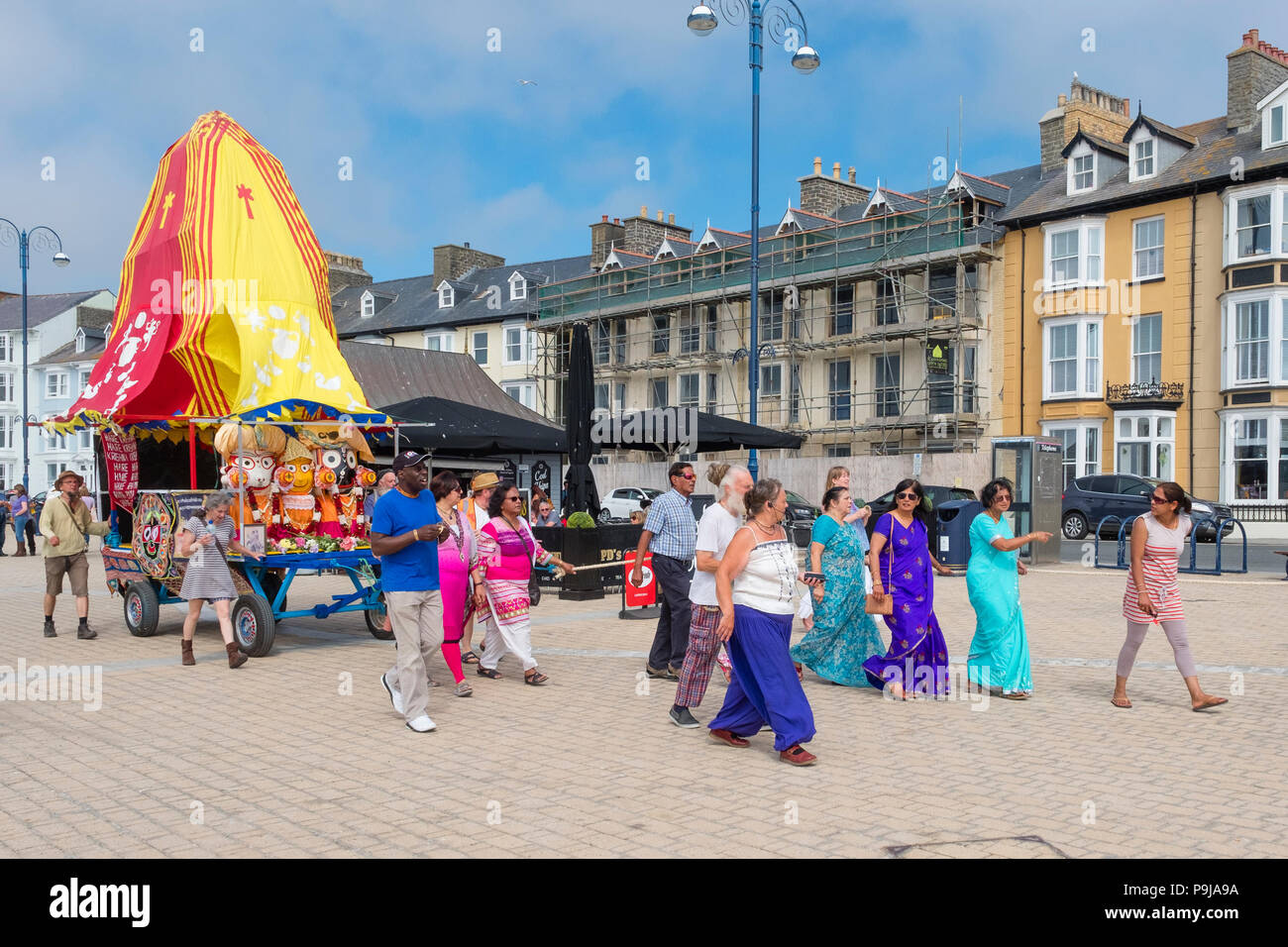 Faith and religion on the UK: A group of Hare Krishna devotees with their 'Ratha' a  colourful votive mobile temple chariot to the deity Lord Jagannath, chanting as they tow it along the promenade at Aberystwyth, Wales UK, on a summer afternoon Stock Photo