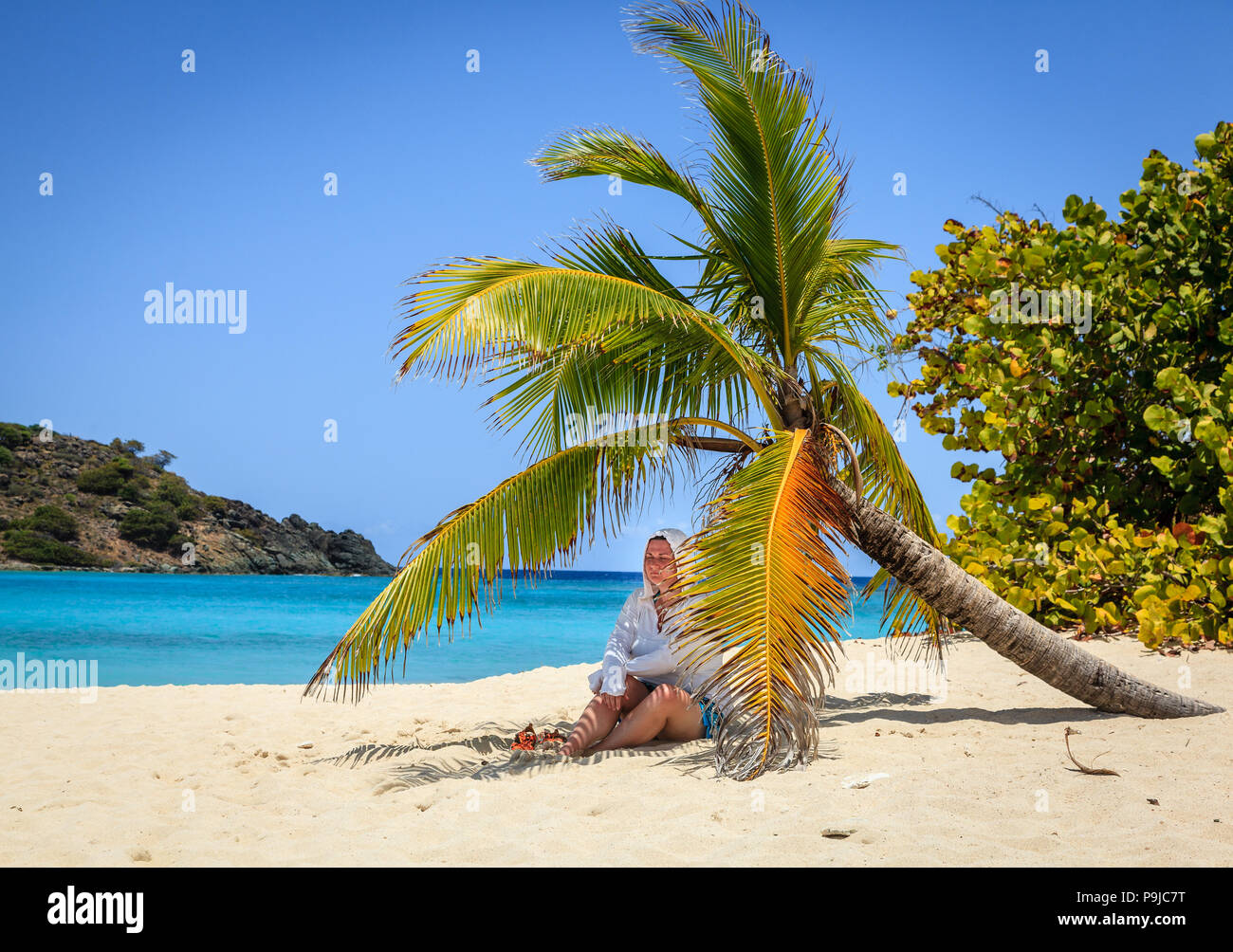 Woman is resting in shade of a palm tree on a beach in British Virgin Islands Stock Photo