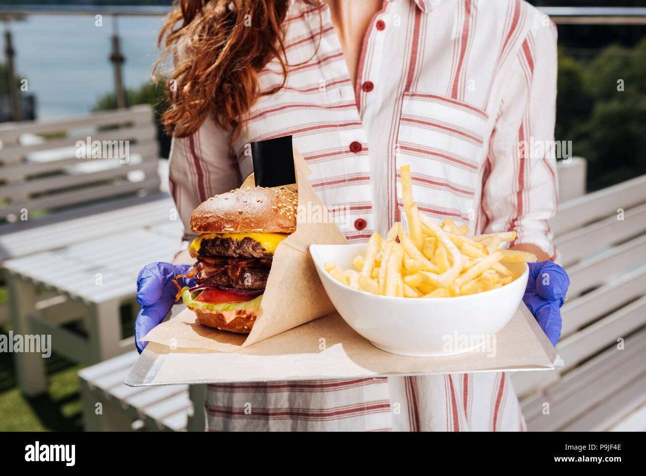 Dark-haired woman wearing white blouse holding burger with fries Stock Photo