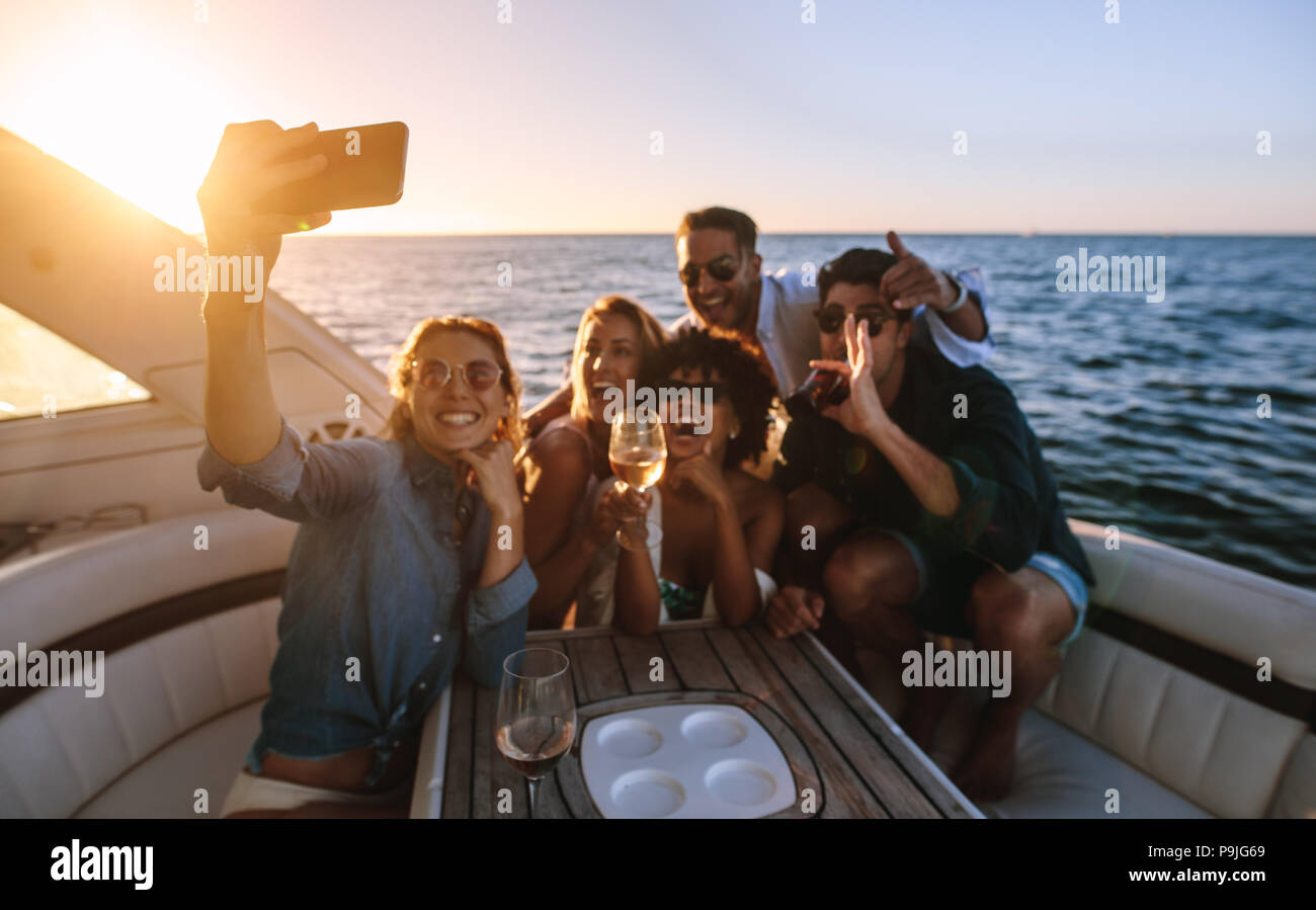 Cheerful young people posing for a selfie at boat party. Crazy friends enjoying a party on private yacht and taking selfie. Stock Photo