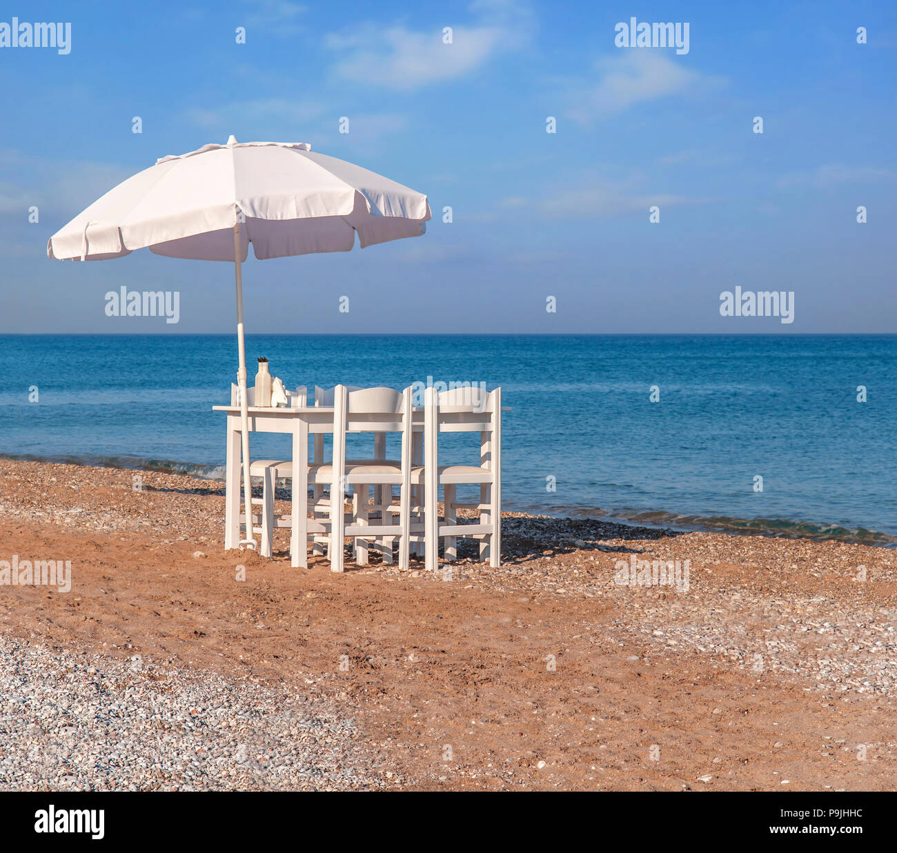 White wooden table on beach with blue sea with four chair and umbrella