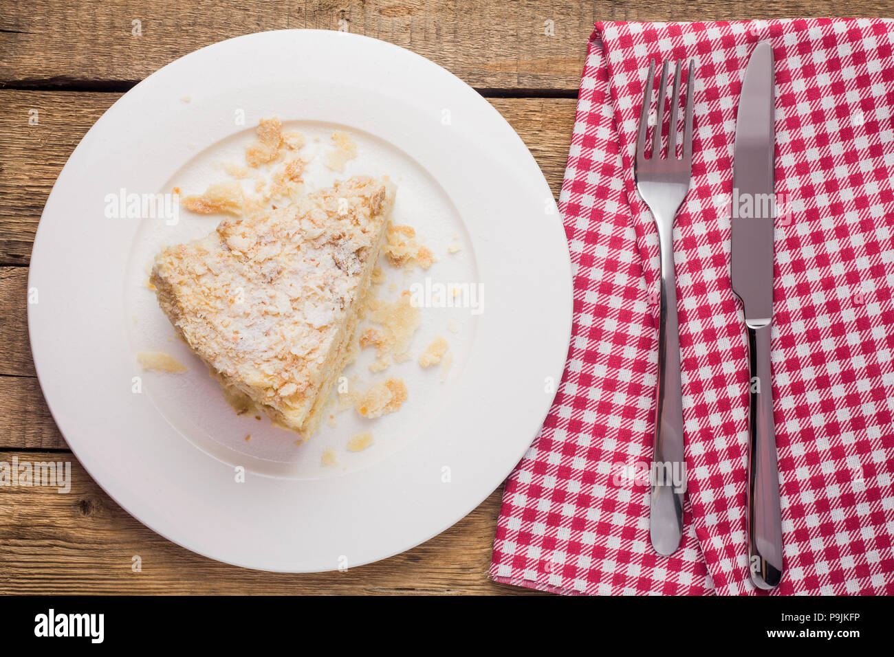 cake Napoleon on a white plate, on a wooden background and a red Stock Photo
