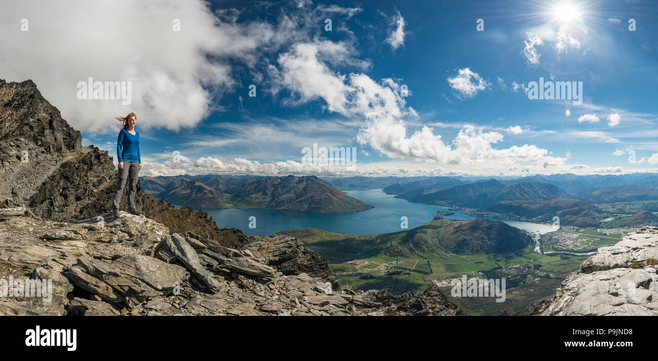 Female hiker standing on rocks on mountain range the Remarkables, overlooking Lake Wakatipu, mountains and Queenstown Stock Photo