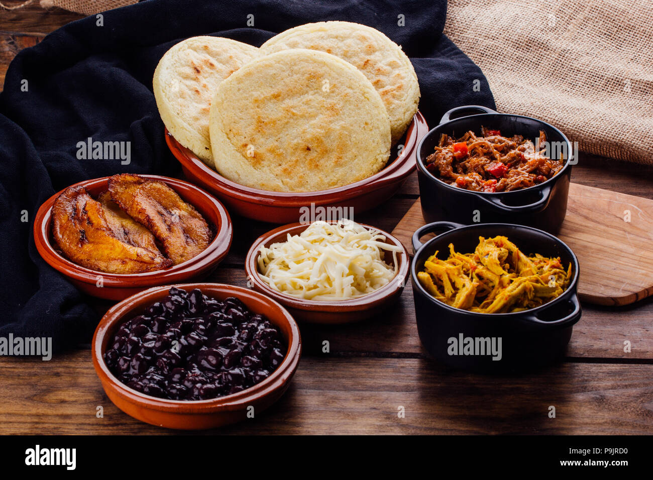 ingredients to fill Venezuelan arepas, mechada meat, chicken, black beans, fried plantain and cheese on a wooden rustic table Stock Photo