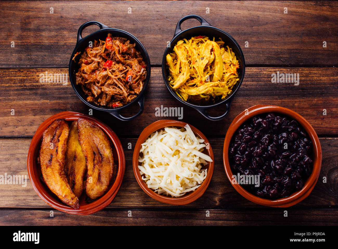 ingredients to fill Venezuelan arepas, mechada meat, chicken, black beans, fried plantain and cheese on a wooden rustic table Stock Photo