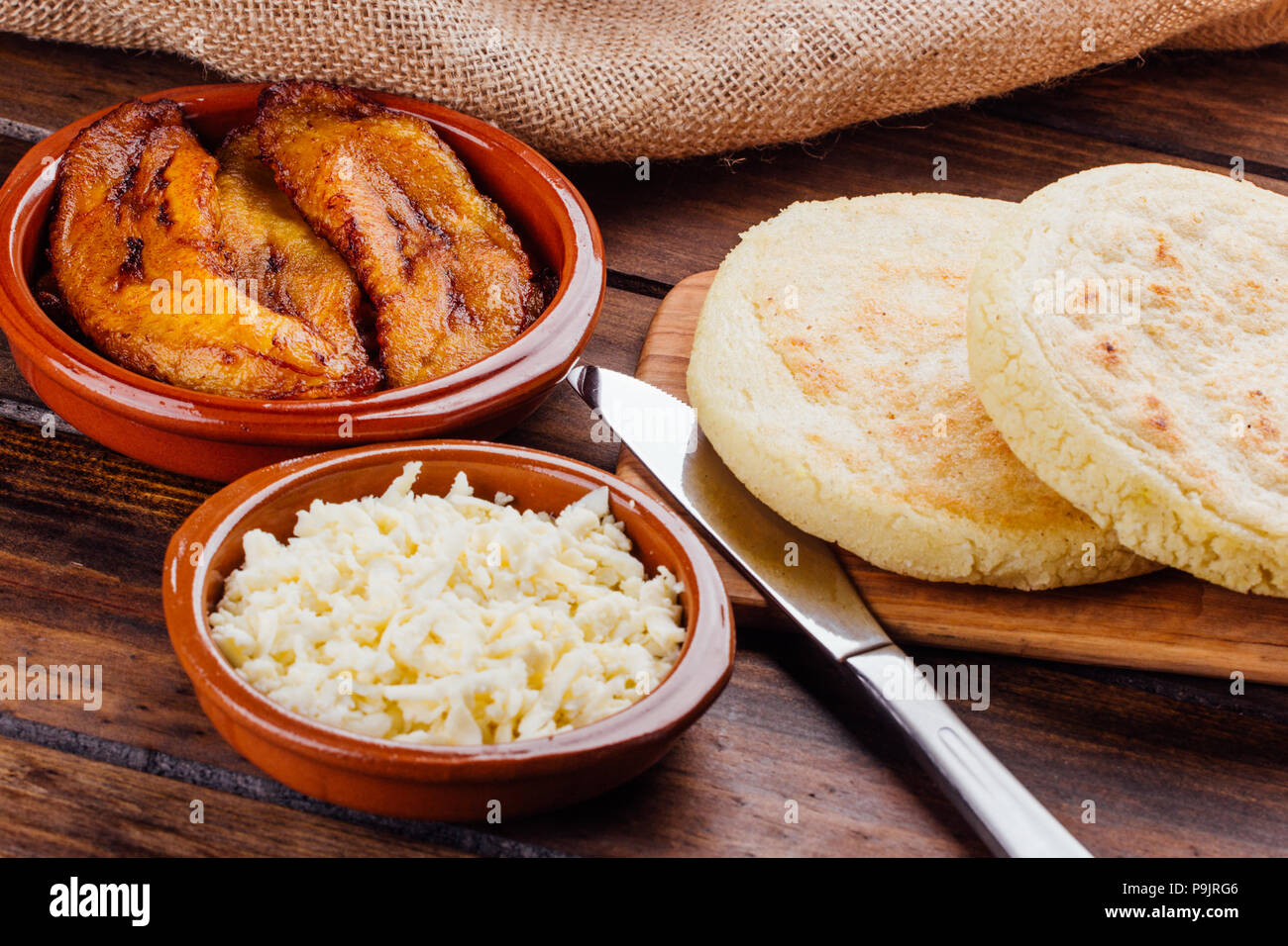 Venezuelan breakfast, Arepas on wooden board and next to it a container with cheese and another with fried plantain to fill Stock Photo