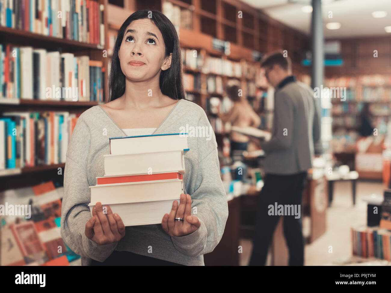 Sad young Brazilian girl holding pile of books in bookstore Stock Photo ...