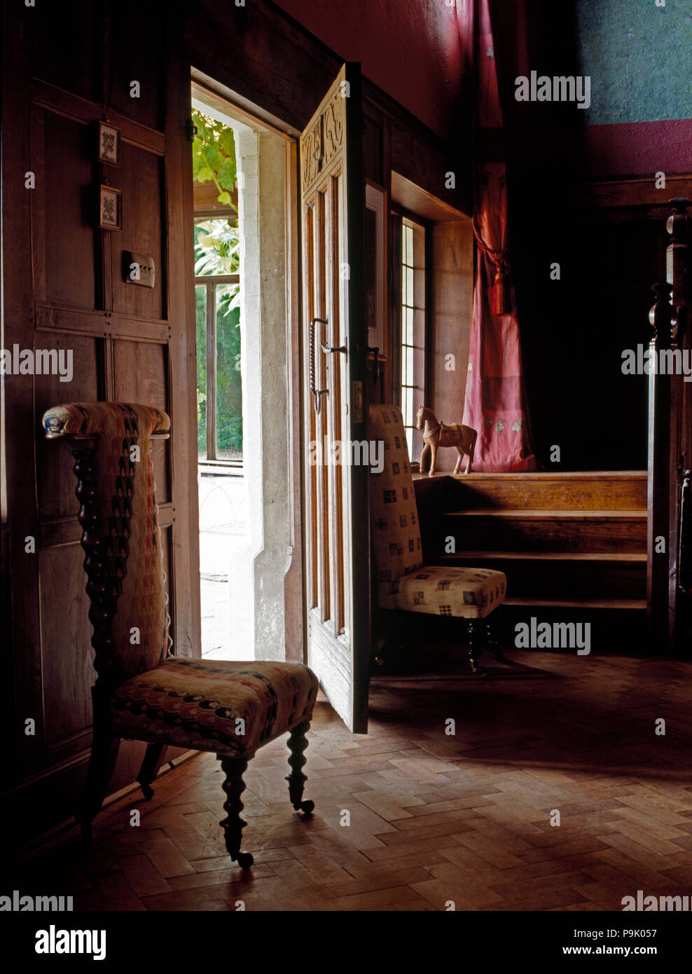 Antique upholstered chair beside open front door in country hall with parquet flooring Stock Photo