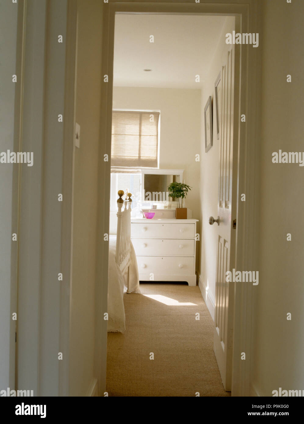 View through open door of small white bedroom with a cream carpet and a white painted chest of drawers Stock Photo