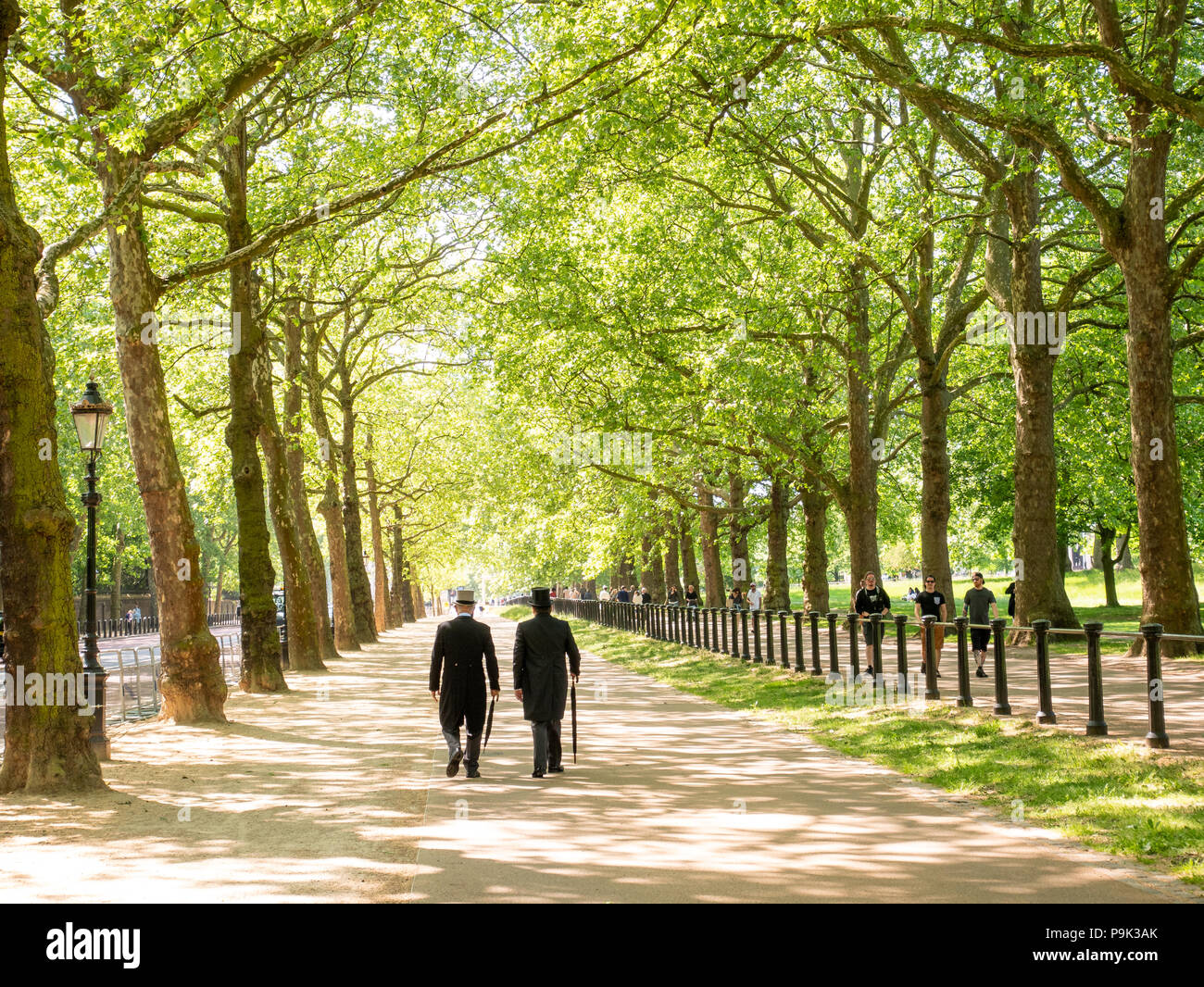 Men in morning suit and top hats strolling down Constitution Hill alongside Green Park, London, UK Stock Photo