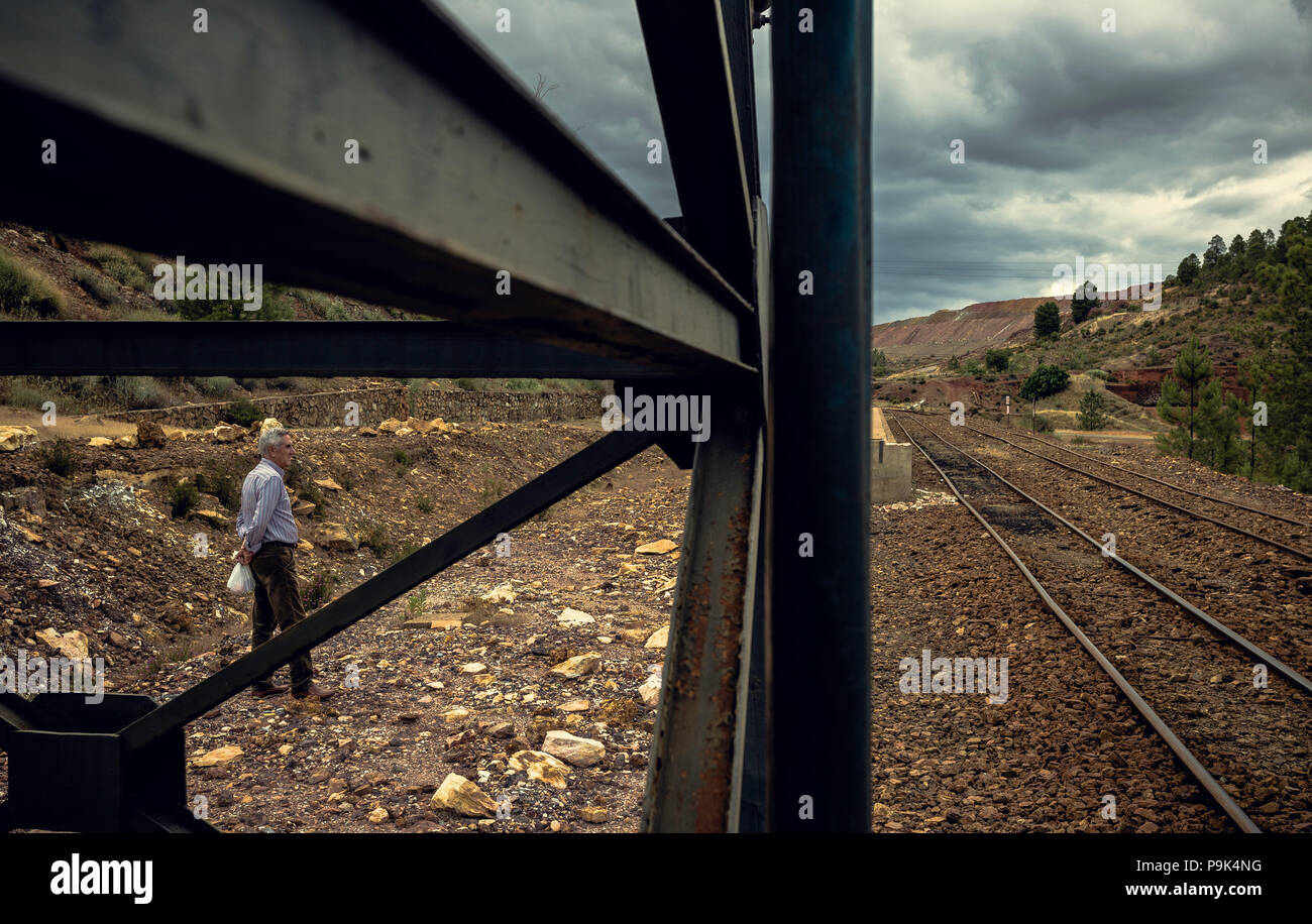 Old man standing and sideways looking at the mining landscape between the irons in the Zaranda mines located between the towns of Nerva and Riotinto,  Stock Photo