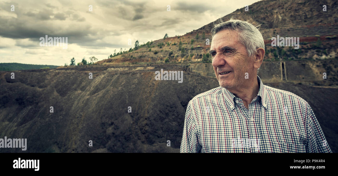 Side portrait of an elderly man smiling with white hair and plaid shirt, with the Zaranda mines in the background, Spain Stock Photo