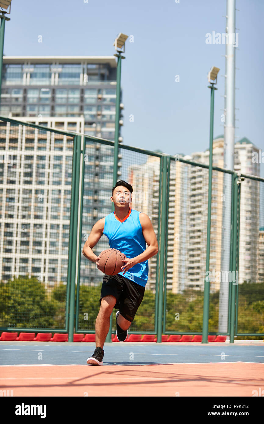 young asian male player playing basketball on outdoor court. Stock Photo