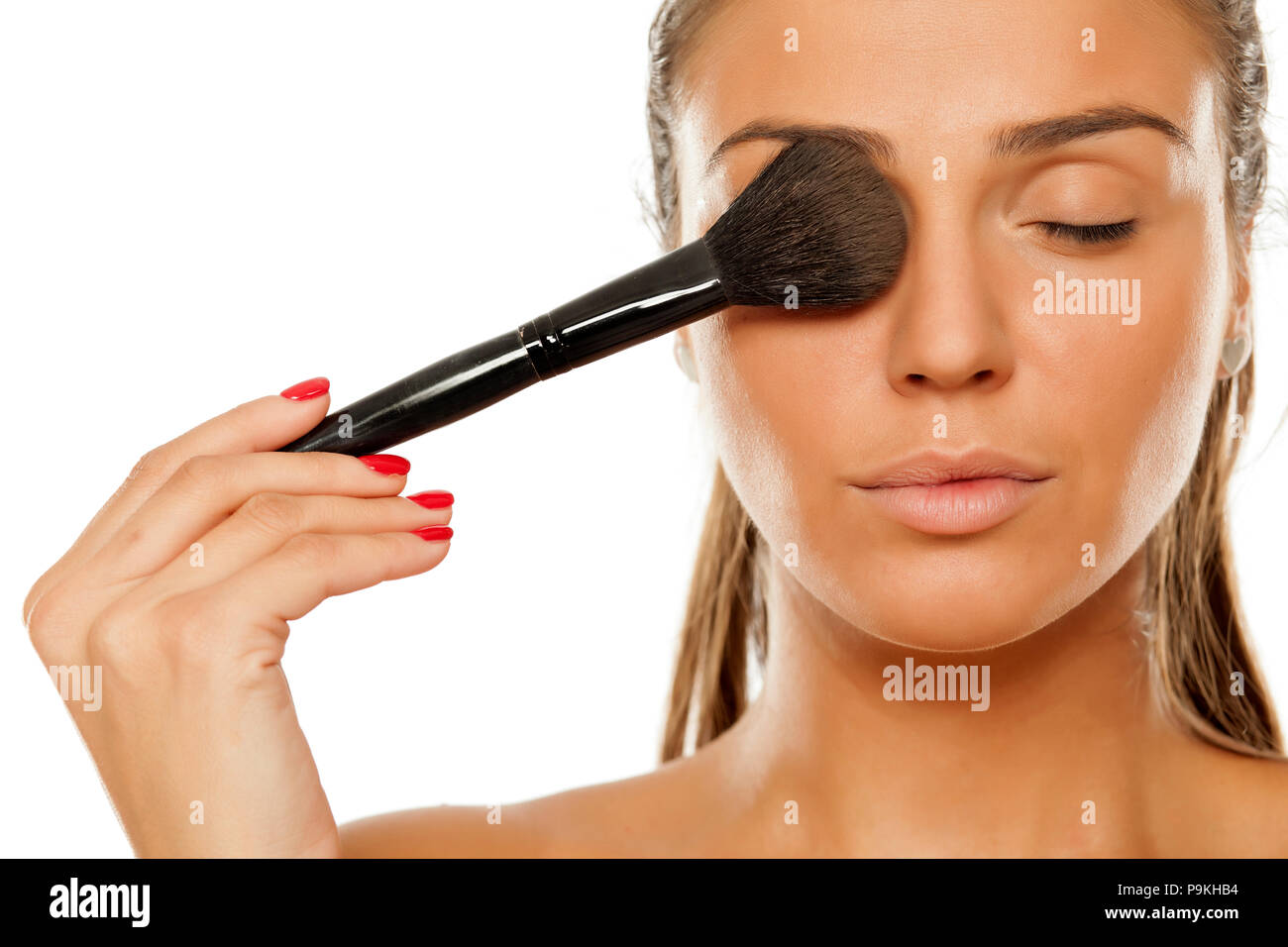 Young woman applying a powder foundation with brush on her face Stock