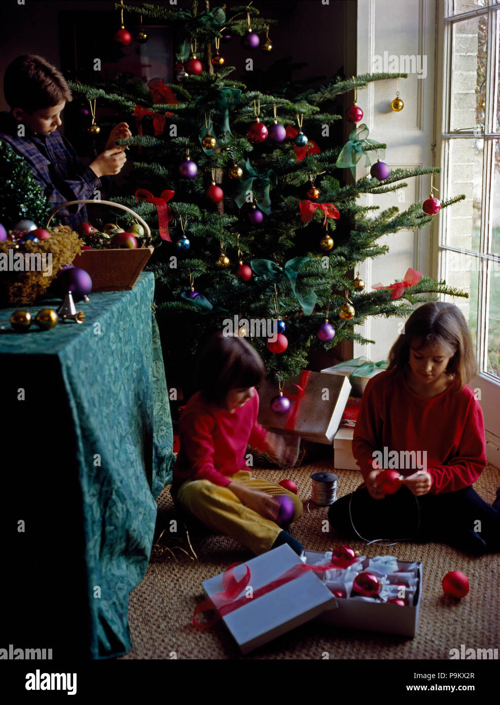 Two small girls opening Christmas presents beside a decorated tree Stock Photo