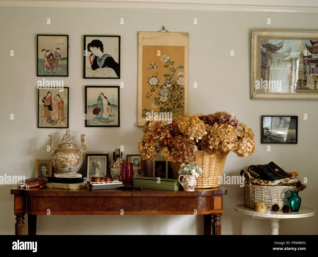 Oriental pictures on wall above antique table with basket of dried hydrangeas Stock Photo