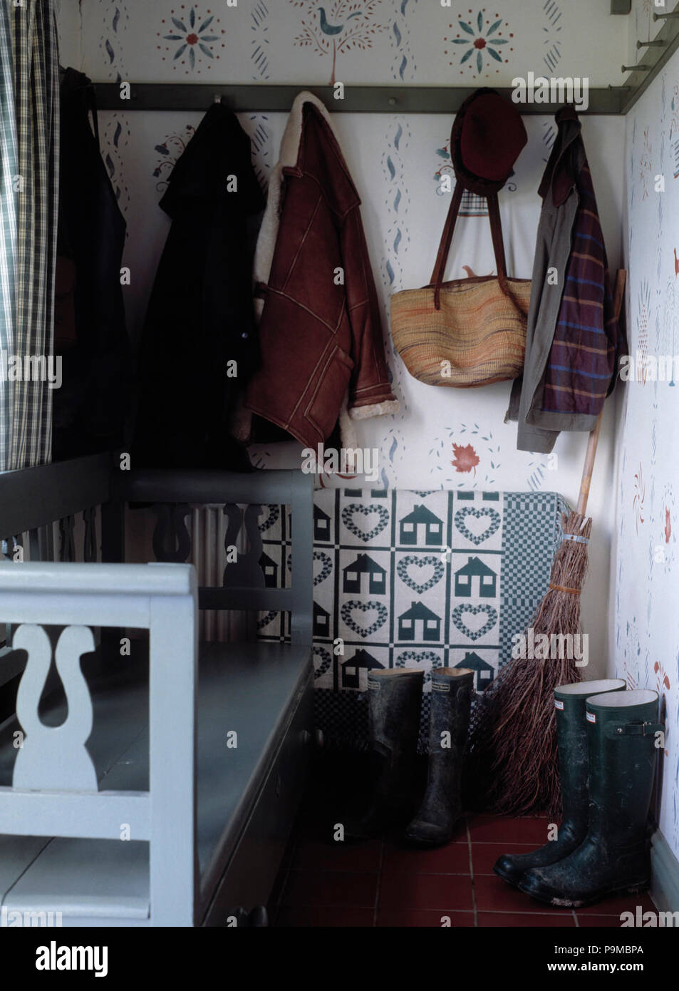 Clothes and bags hanging on peg-rail above Wellington boots in small cottage hall with pale blue wooden settle Stock Photo