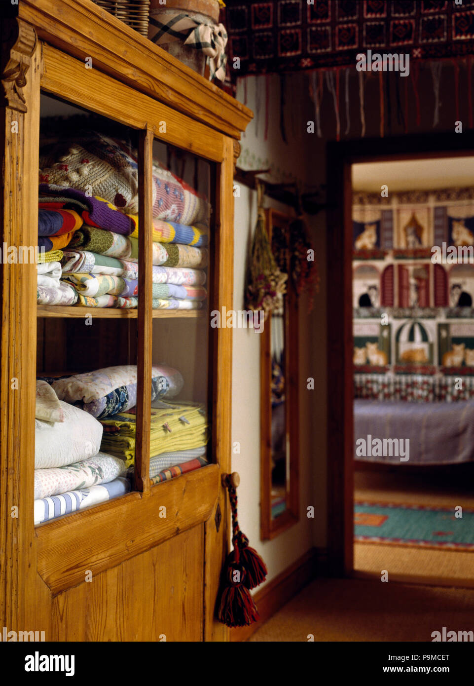 Folded quilts in a glass front cupboard in an nineties country hall Stock Photo