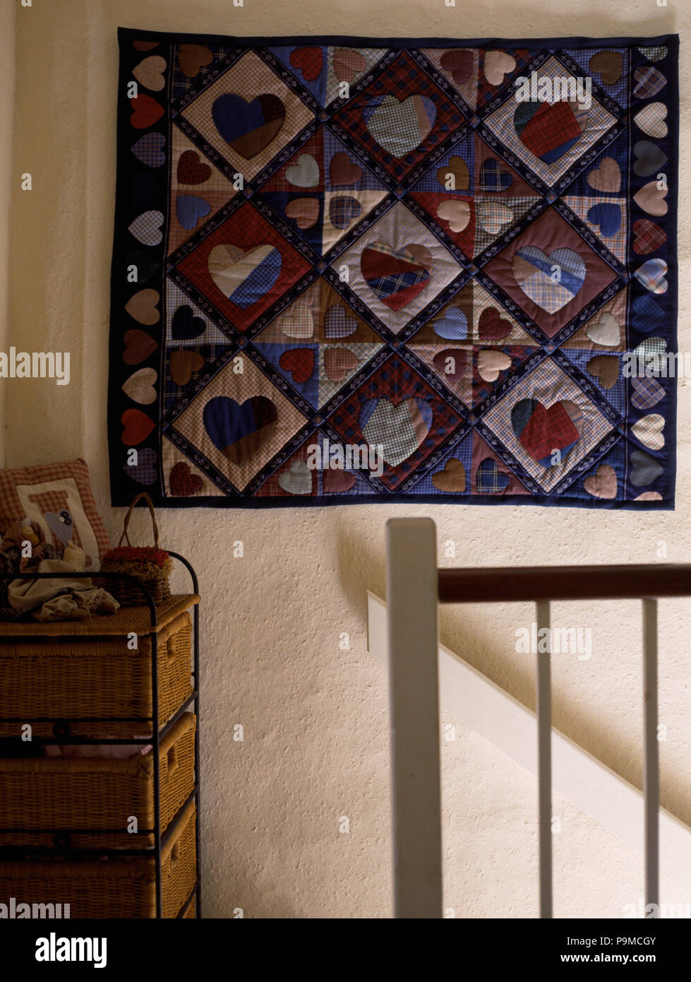 Heart-motif patchwork wall-hanging above staircase in cottag landing Stock Photo
