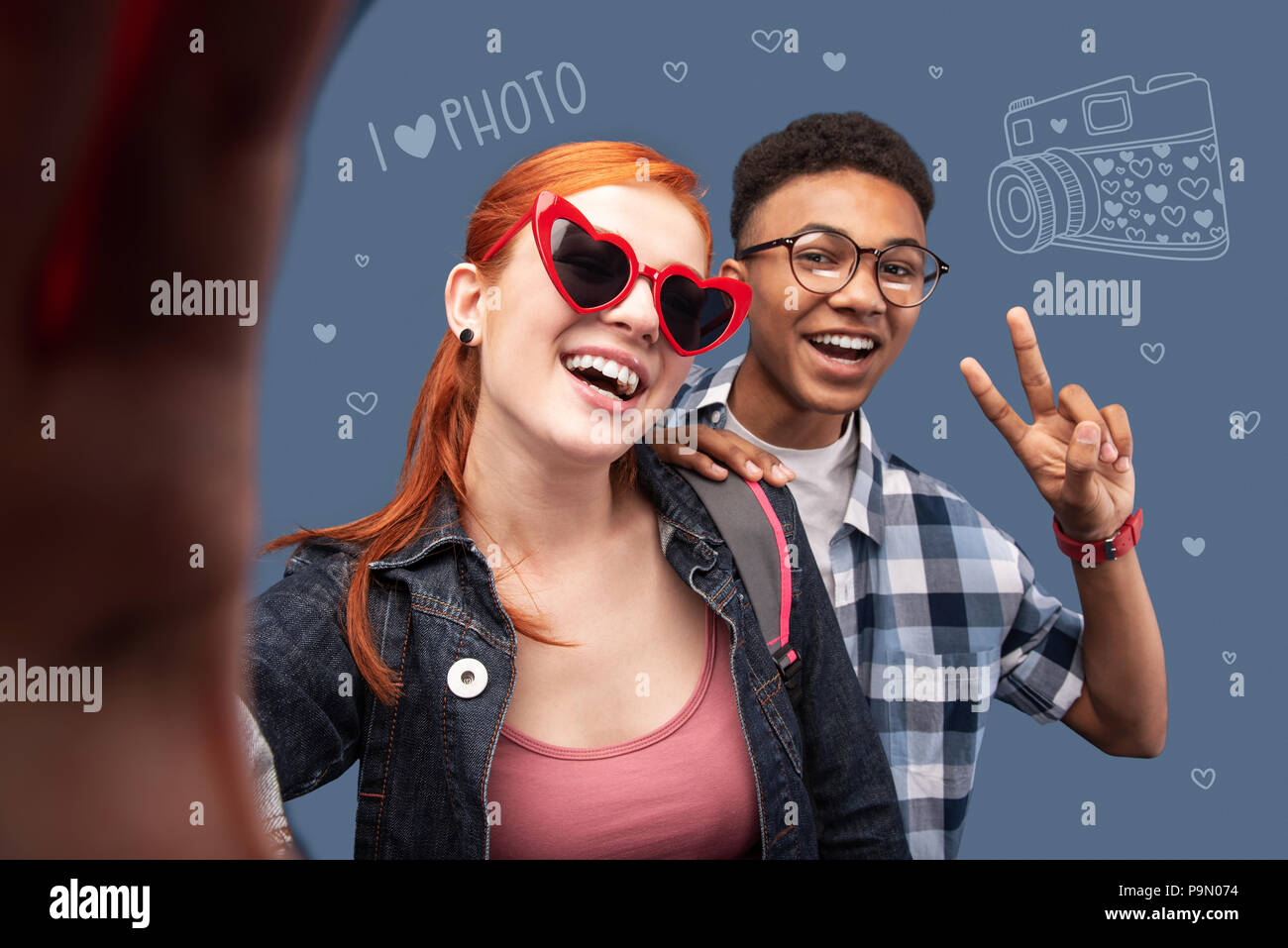 Happy teenager making a peace sign while taking a selfie with his friend Stock Photo