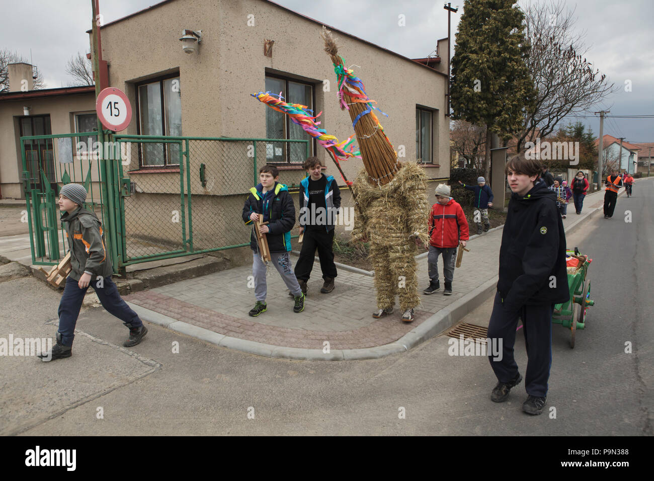 Traditional Easter procession known as Vodění Jidáše (Marching Judas) in the village of Stradouň in Pardubice Region, Czech Republic. A person dressed in a straw suit representing Judas marches through the village escorted with boys twisting ratchets and with a teenage boy who carries a cart for donations during the procession on 31 March 2018. Early in the morning on Holy Saturday, the eldest teenage boy in the village is dressed in a ridiculous straw suit. He is supposed to perform Judas Iscariot in this way. Wearing this obscure outfit, he has march through the village from house to house e Stock Photo