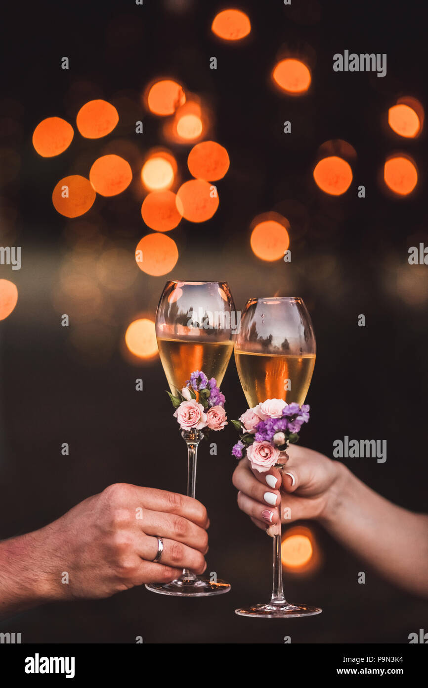 Two glasses of champagne in couple hands decorated with fresh flowers