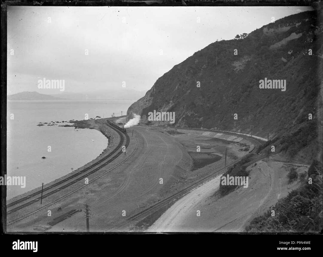 323 View of a train rounding Rocky Point in 1908 after the track was moved nearer the harbour following partial reclamation, between Wellington and Petone. ATLIB 277762 Stock Photo