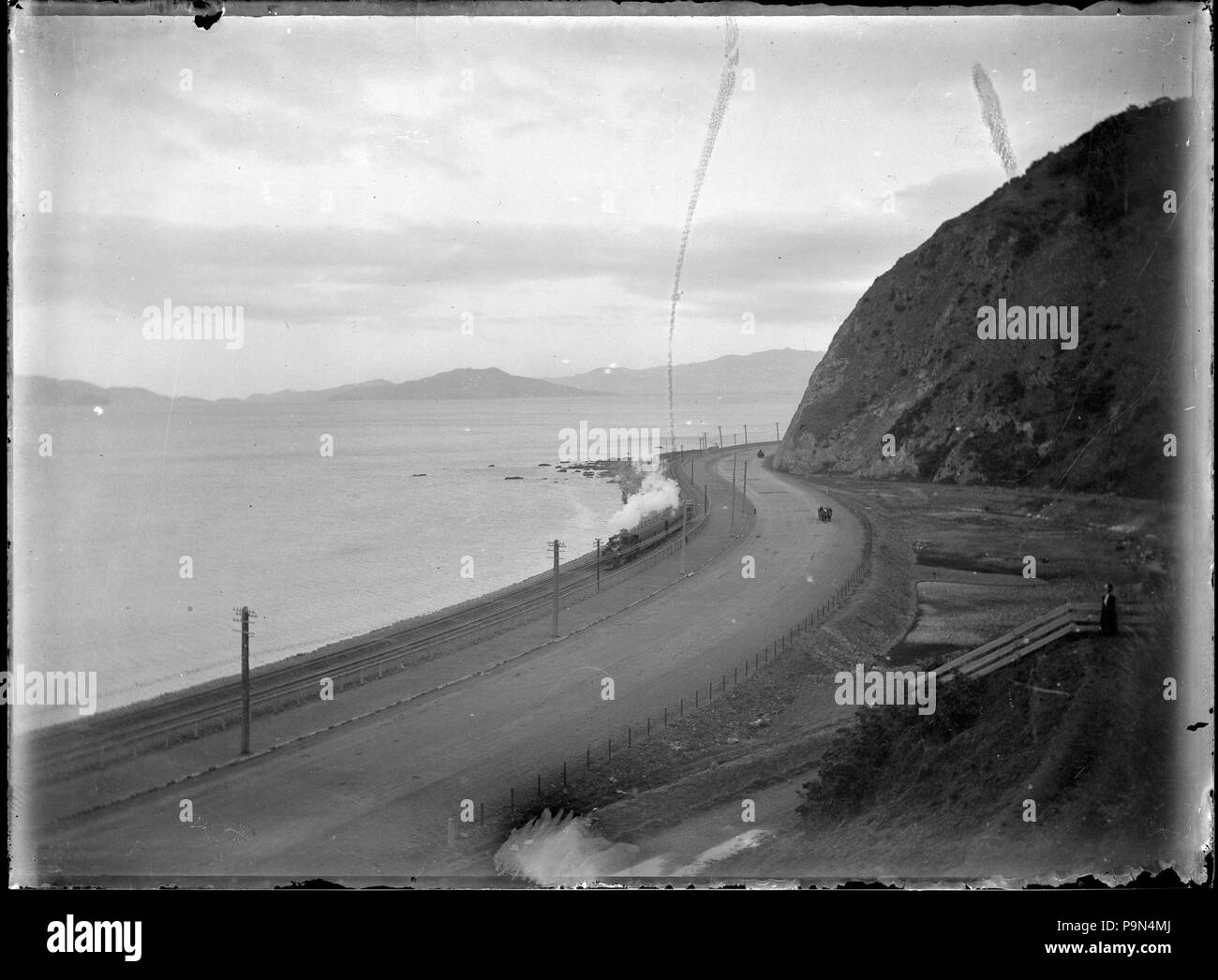 323 View of a train rounding Rocky Point after the track was moved nearer the harbour following partial reclamation, between Wellington and Petone. ATLIB 277763 Stock Photo