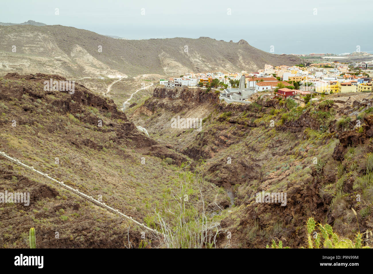 View of Barranco del Infierno (Hell's Gorge) showing the valley or canyon with the town of Adeje above with bright buildings, Atlantic Ocean, green Stock Photo
