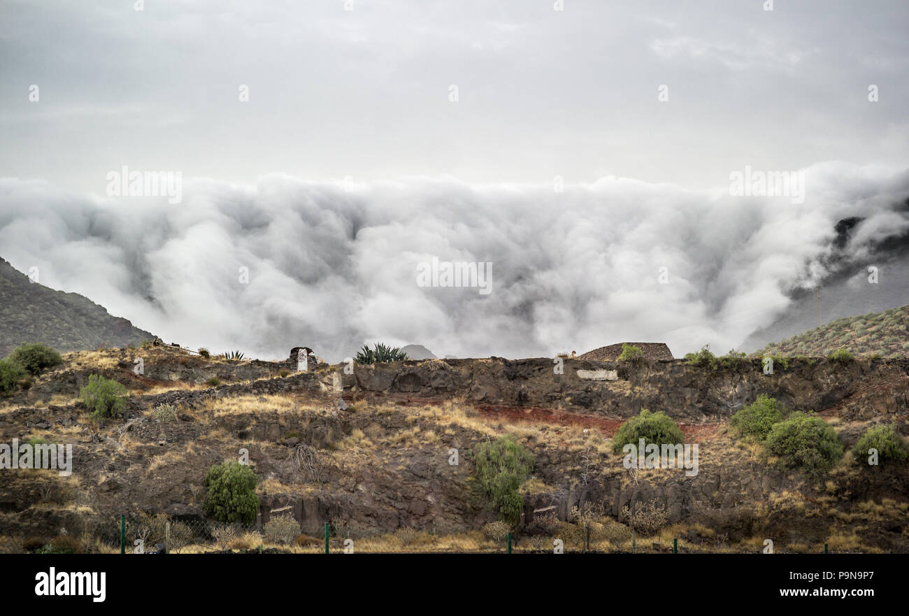 Remarkable landscape ornographic waterfall clouds spilling over the leeward slope of mountains north of Santa Cruz, Tenerife. Unusual nature. Stock Photo