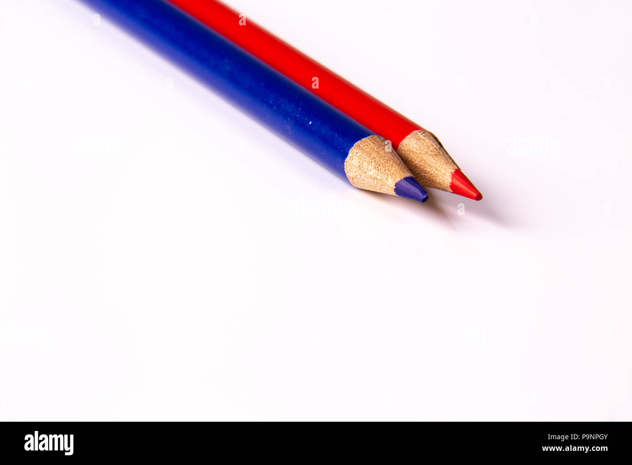 Red and blue contrasting color pencils on white reflective acrylic. Stock Photo