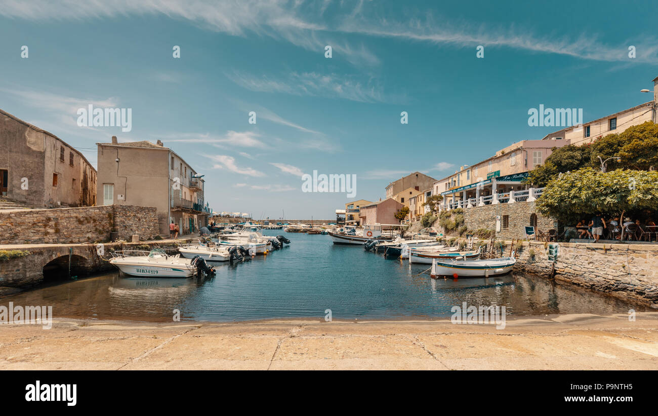 CENTURI, CORSICA - 10th JULY 2018. Fishing boats moored in the small harbour at Centuri on Cap Corse in Corsica surrounded by bars and restaurants Stock Photo