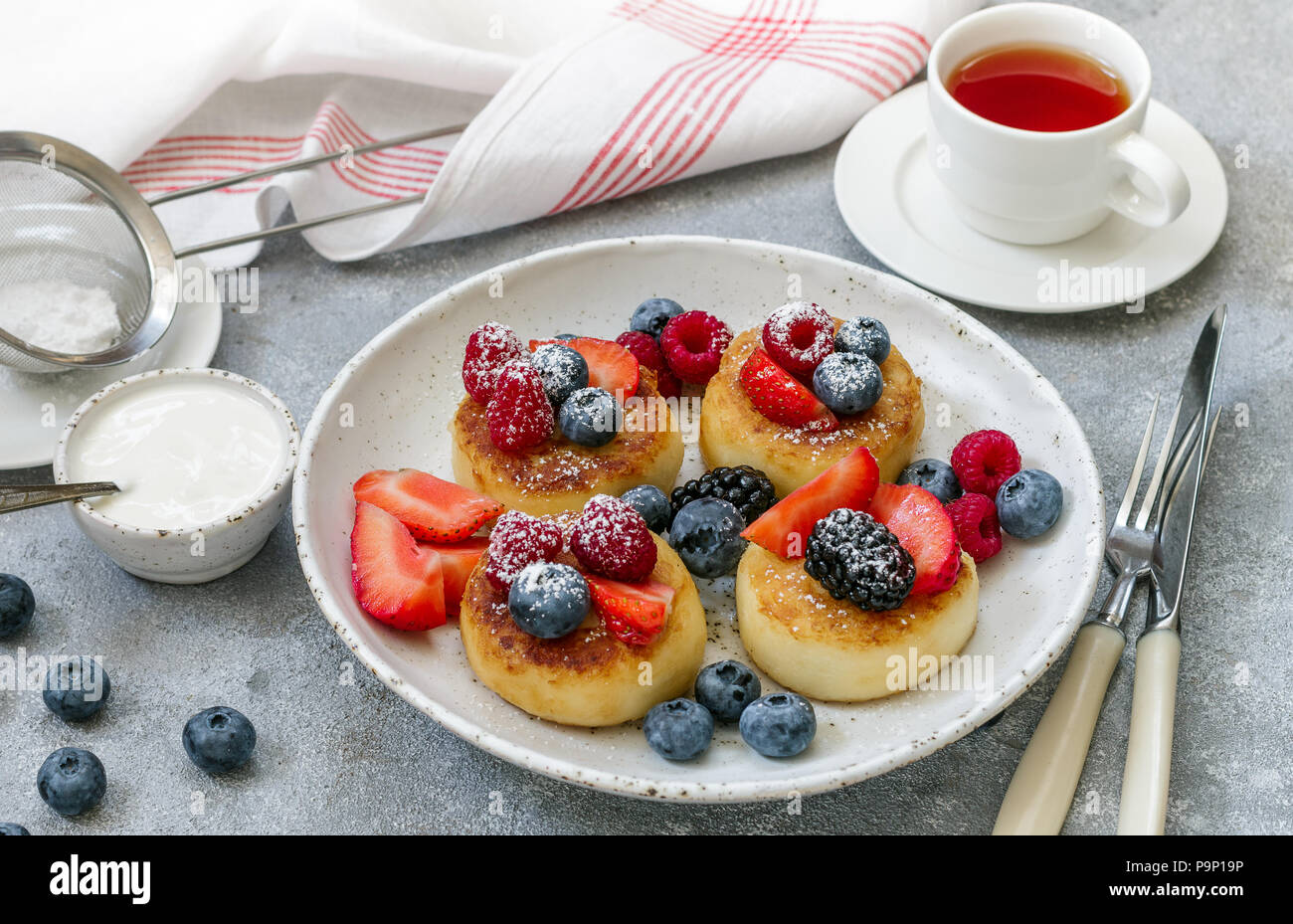 Cottage cheese pancakes, syrniki, curd fritters with fresh berries (raspberry, strawberry, blueberry, BlackBerry) and powdered sugar in a white plate. Stock Photo
