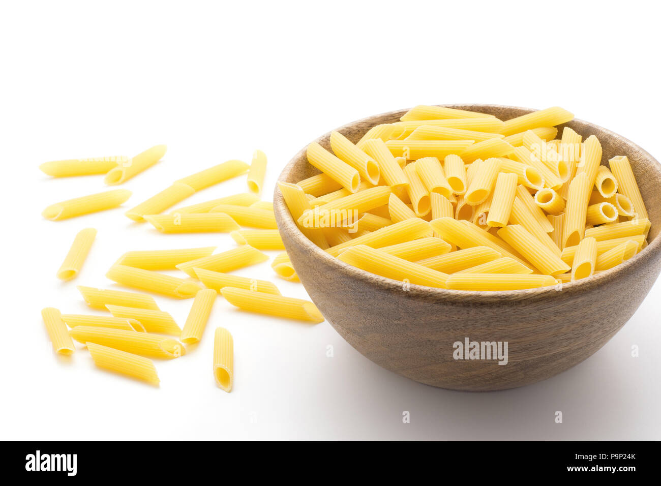 Penne rigate in wooden bowl isolated on white background a lot of dry raw pasta pieces Stock Photo