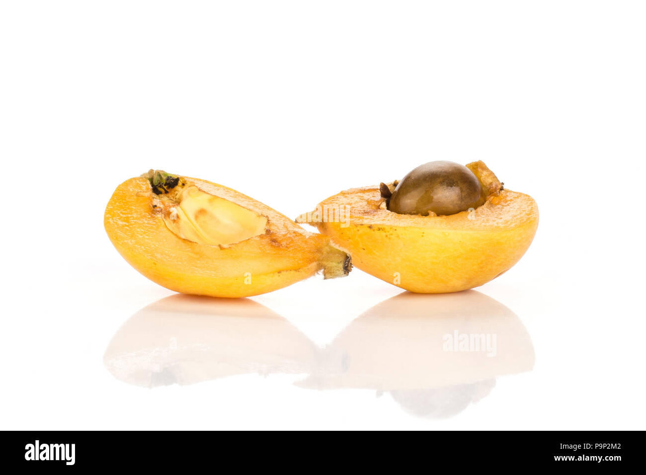 Two fresh orange Japanese loquat halves with a seed isolated on white