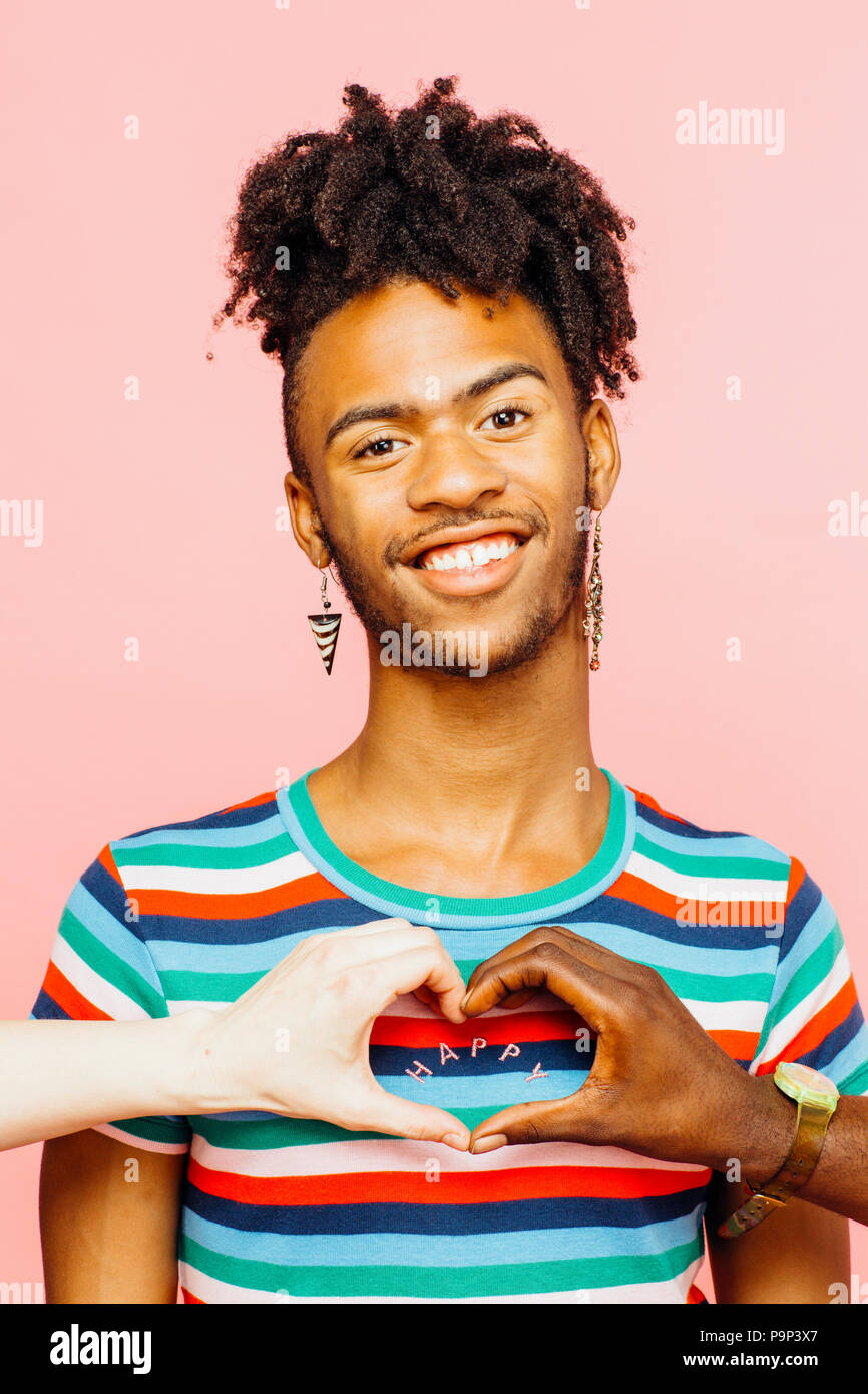 Portrait of a smiling man with earrings and heart shaped with hands around happy sign on his shir Stock Photo