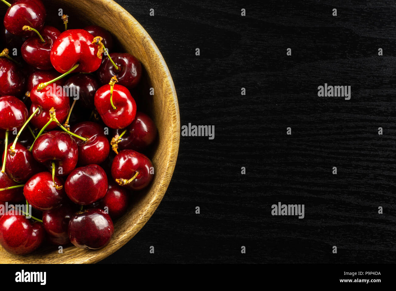 Sweet bright red cherry in a wooden bowl flatlay on black wood Stock Photo