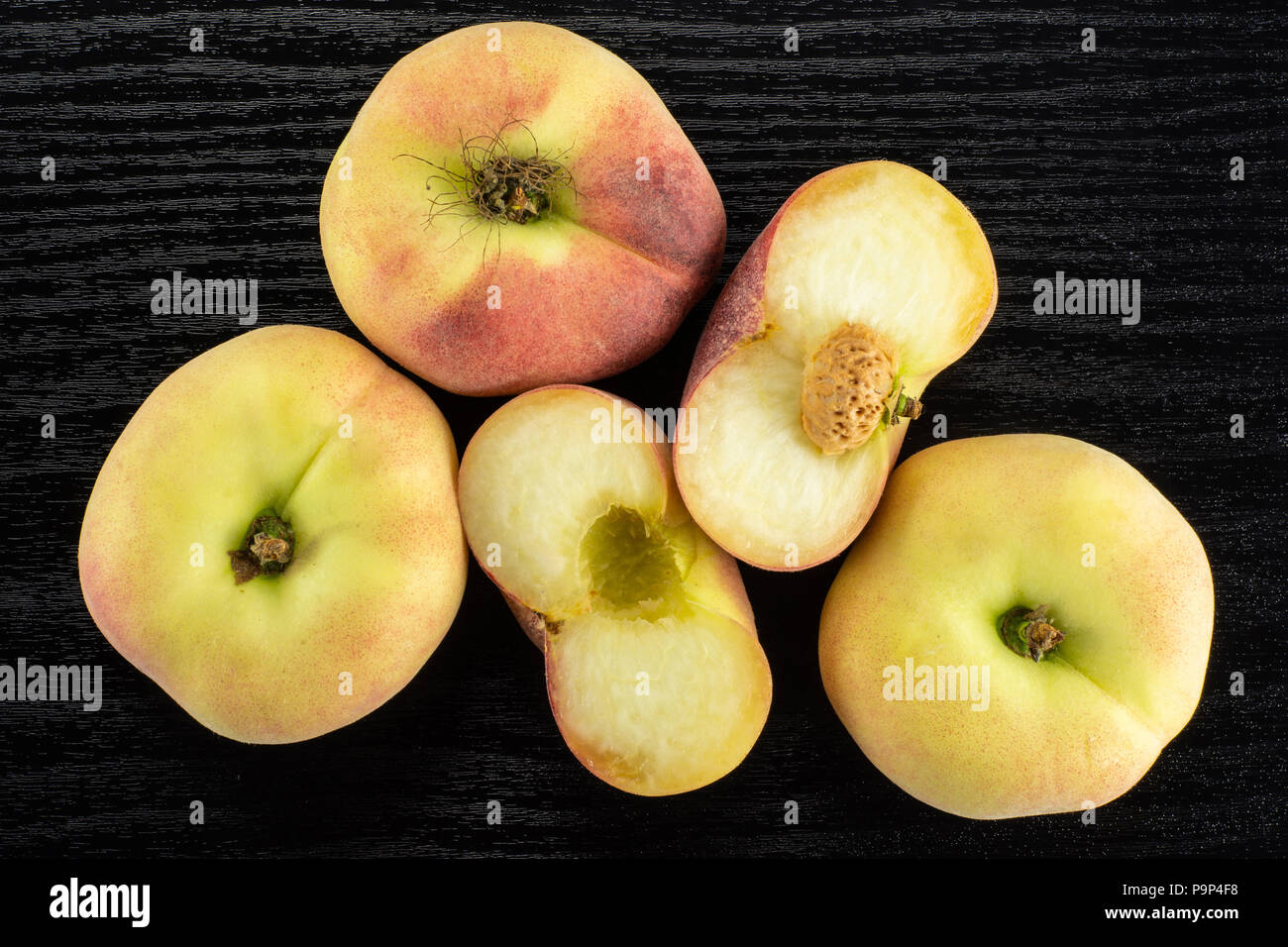 Three fresh ripe Saturn peaches and one cut in two halves top view on