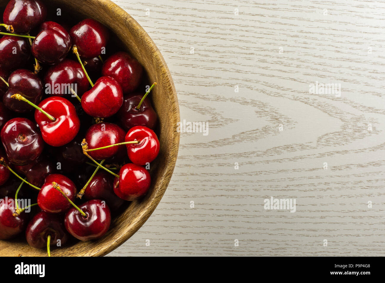 Sweet bright red cherry in a wooden bowl flatlay on grey wood Stock Photo