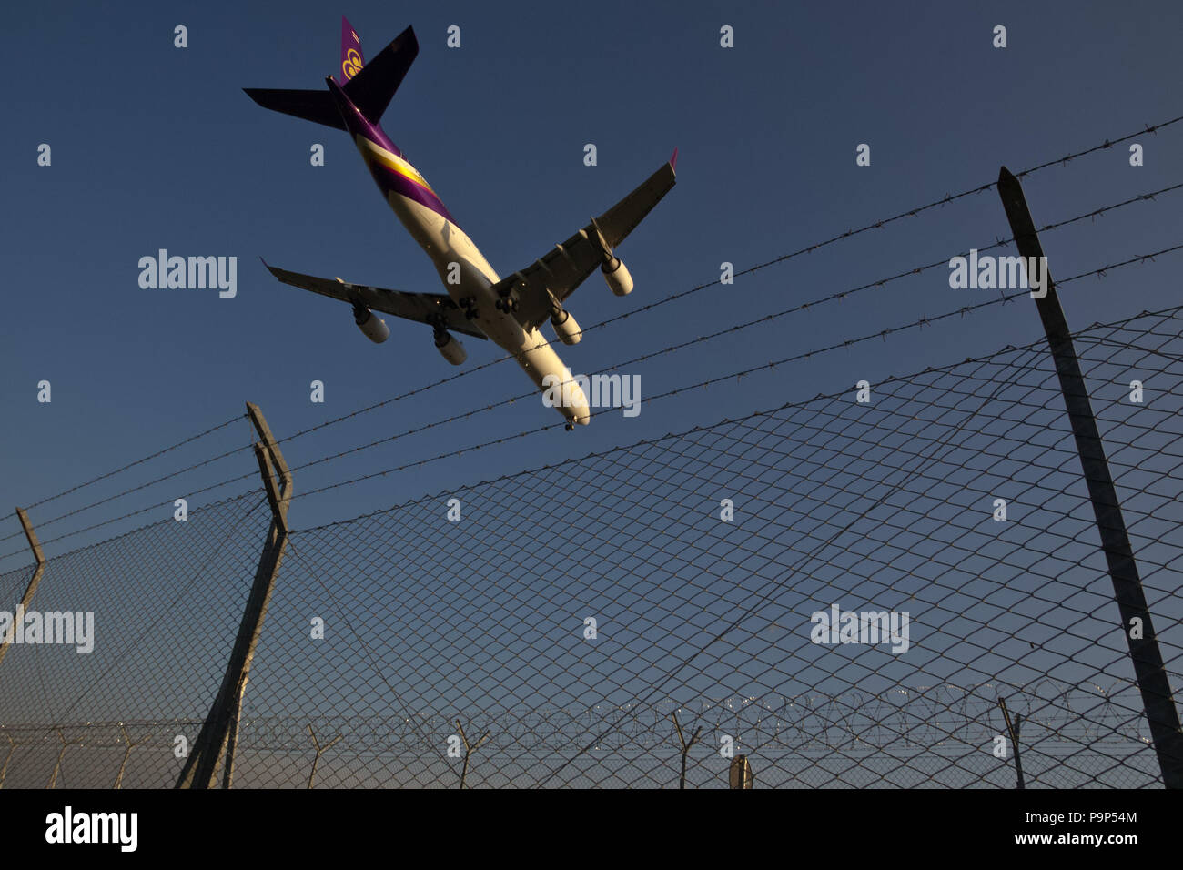 The Airbus A340 civil jet airplane of Thai Airways flies over security fence as it lands at Malpensa International Airport, Milan, Italy Stock Photo