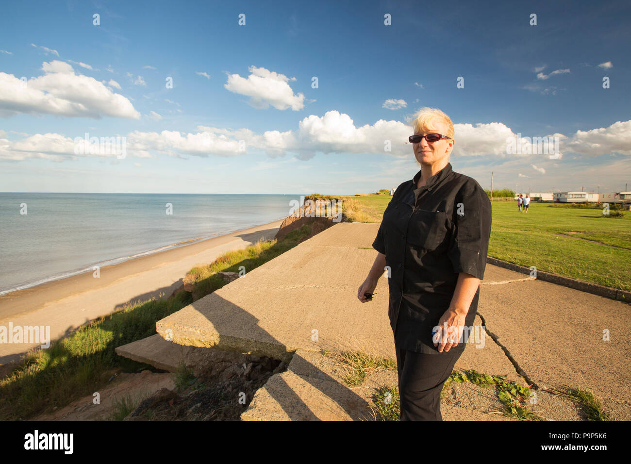 Woman stands next to the edge of collapsing coastal cliffs at Aldbrough on Yorkshires East Coast, UK. She is stood in the location where her house use Stock Photo