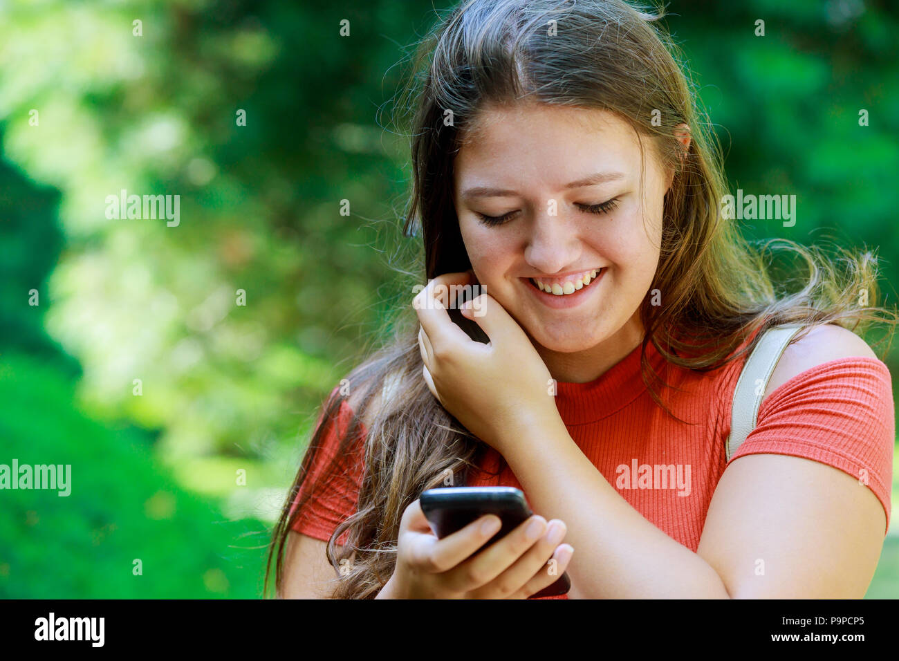 Cute young girl holding smartphone using in summer day in a park smiling and looking at camera. Stock Photo