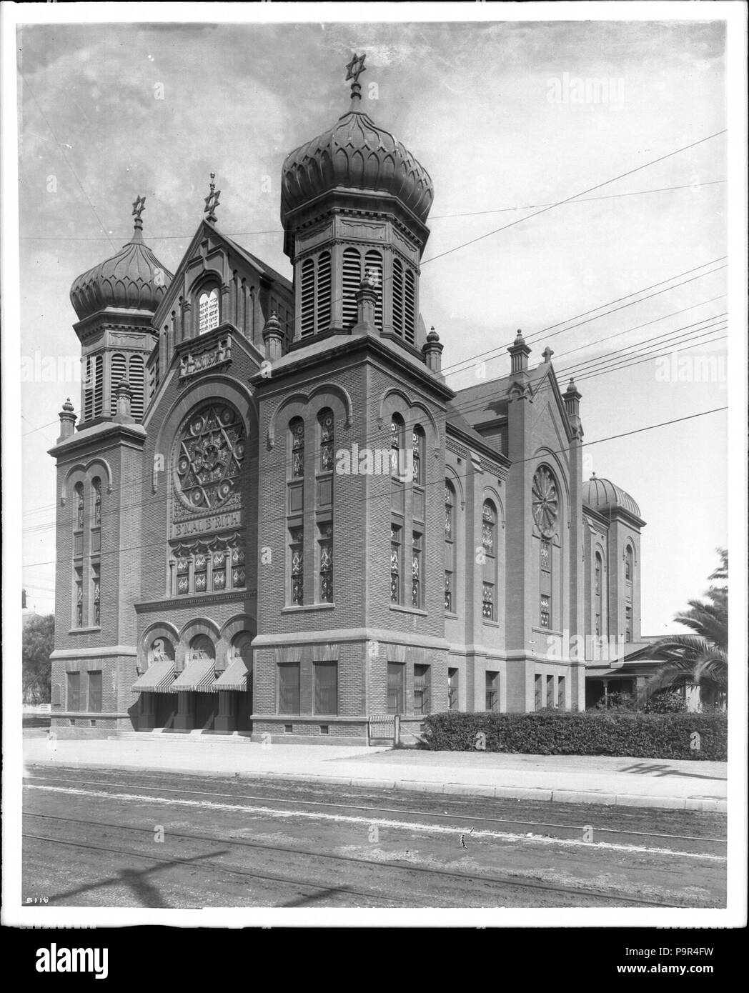 . English: B'nai B'rith Synagogue (Temple), located on Hope and 9th Streets, Los Angeles, ca.1900  Photograph of the B'nai B'rith Synagogue (Temple), view of Hope Street facade, south towards 9th Street, Downtown Los Angeles, ca.1900. Former temple of the present day Wilshire Boulevard Temple Congregation.     The front facade was composed of two square towers with onion dome tops flanking the central aisle. 'B'nai B'rith', the name of the temple, is prominently displayed on the facade, right below the circular stained-glass window where the Star of David embossed in it. Above the circular sta Stock Photo