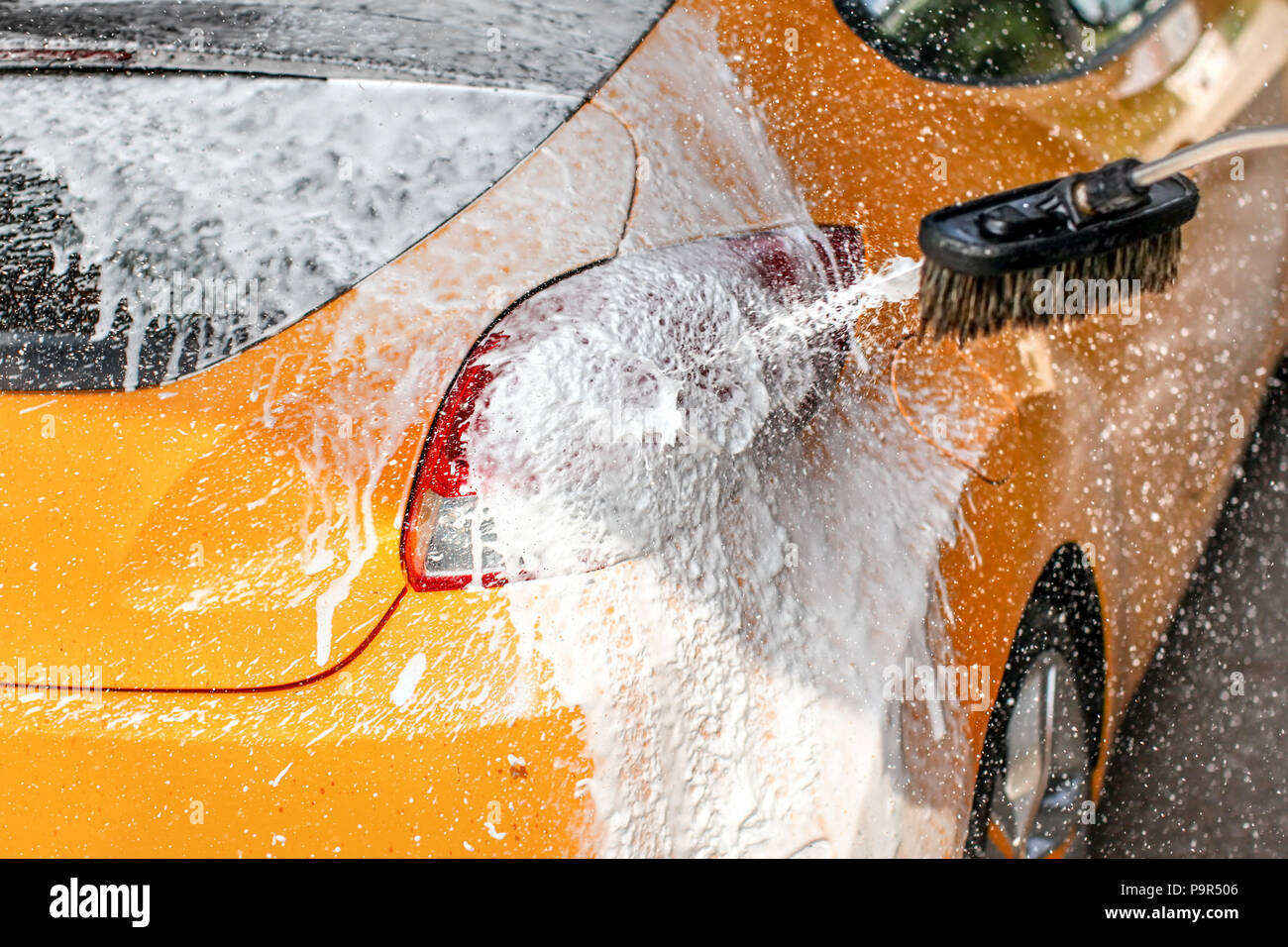 Yellow car washed in carwash soap ad foam spraying drops to sun lit back and rear light Stock Photo Alamy