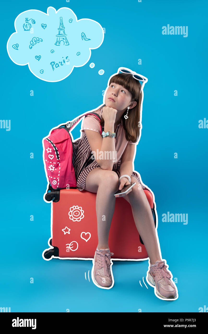 Dreamy girl thinking about Paris while sitting on her luggage Stock Photo